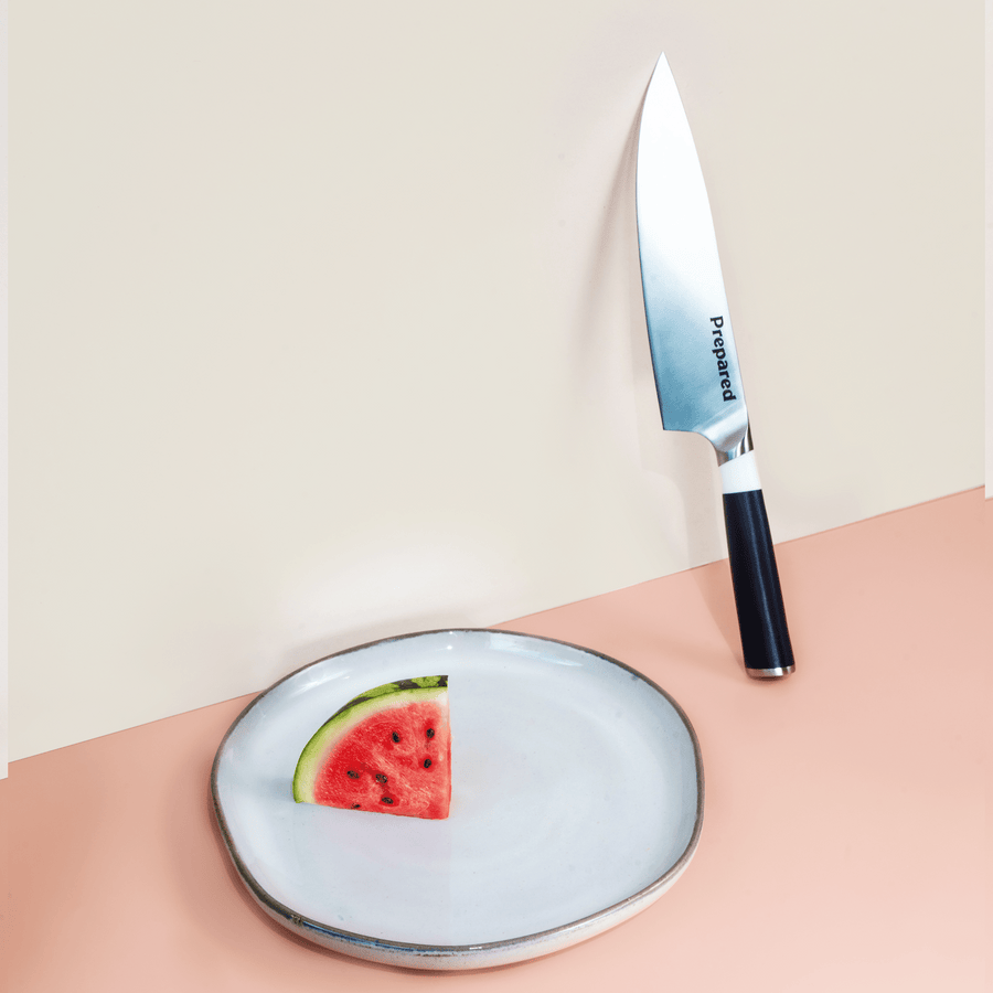 Prepared Chef's knife leaning against a wall, shown in the color ash.