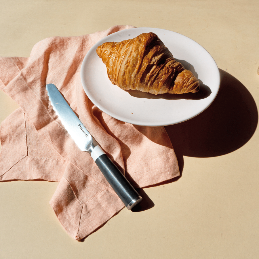 The bread knife in the color ash and a croissant on the table during a bright and sunny Australian day